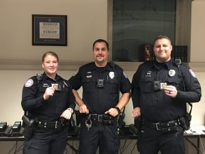 Officers Zaccari, Welling, & Bennett standing together holding up challenge coins